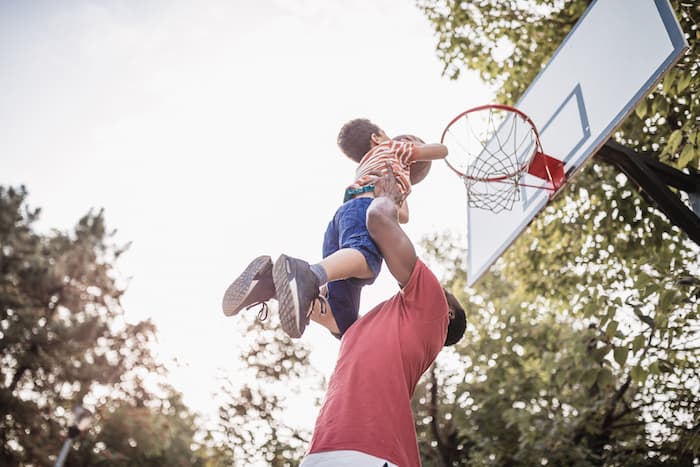 man painlessly hoists young son into air to dunk basket in basketball