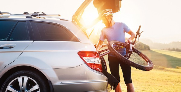 male cyclist loads bicycle into car as sun sets